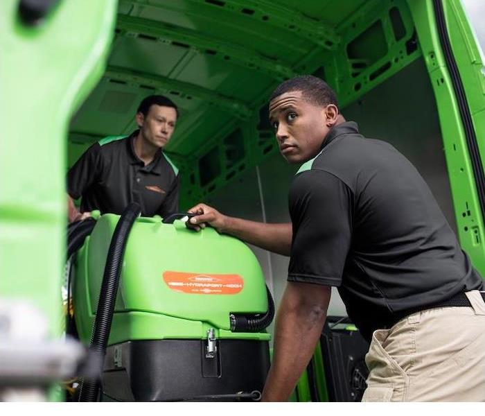 Two SERVPRO employees unloading cleaning equipment out of a green van
